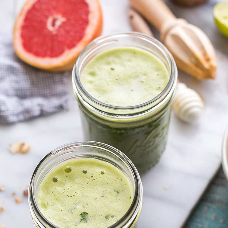 Green juice in mason jars with a grapefruit half and honey dipper in the background.