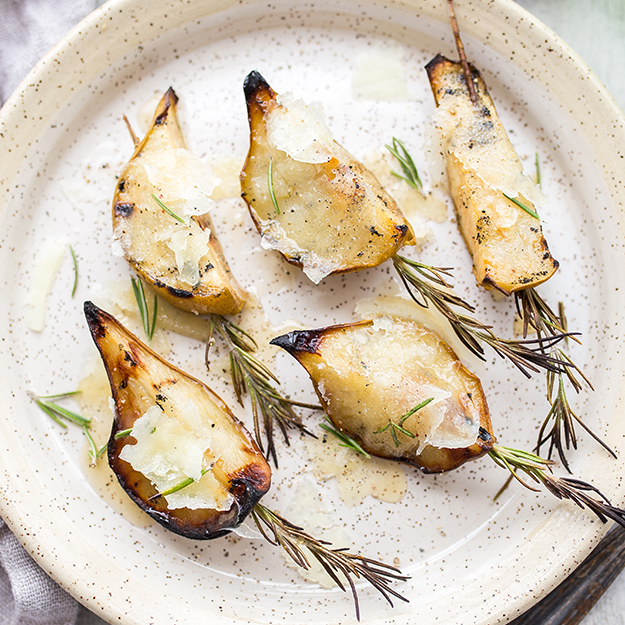Roasted pears with Manchego cheese, honey drizzle and rosemary on a speckled ceramic plate.
