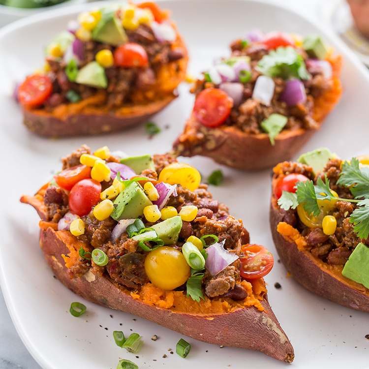Sweet potatoes stuffed with bison and vegetables, on a white plate.