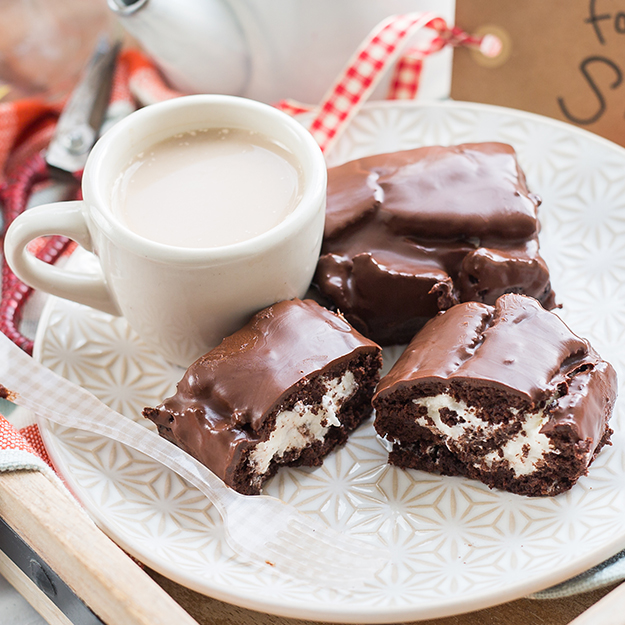 Chocolate-covered marshmallow treats on a patterned plate with a cup of milk.