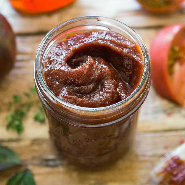 Barbeque sauce in a jar on a rustic wooden table with fresh tomatoes and herbs.