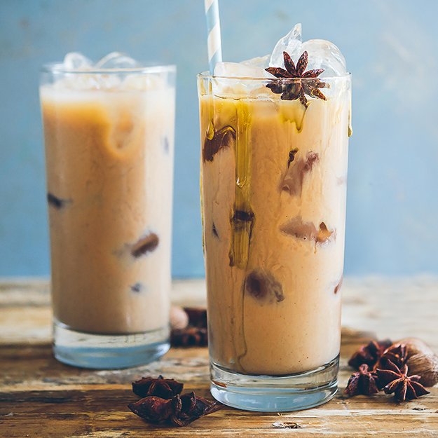 Iced spiced chai drink in tall glasses with star anise and honey drizzle, rustic wood backdrop.