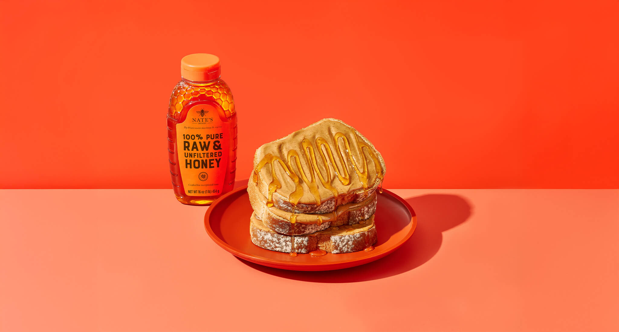 Three slices of peanut butter toast stacked with honey drizzled all over toast stack. Next to Nate's honey bottle.