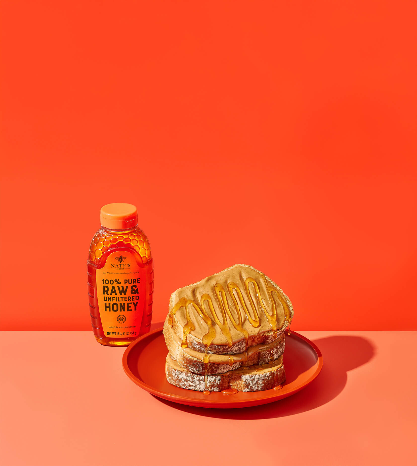 Three slices of peanut butter toast stacked with honey drizzled all over toast stack. Next to Nate's honey bottle.