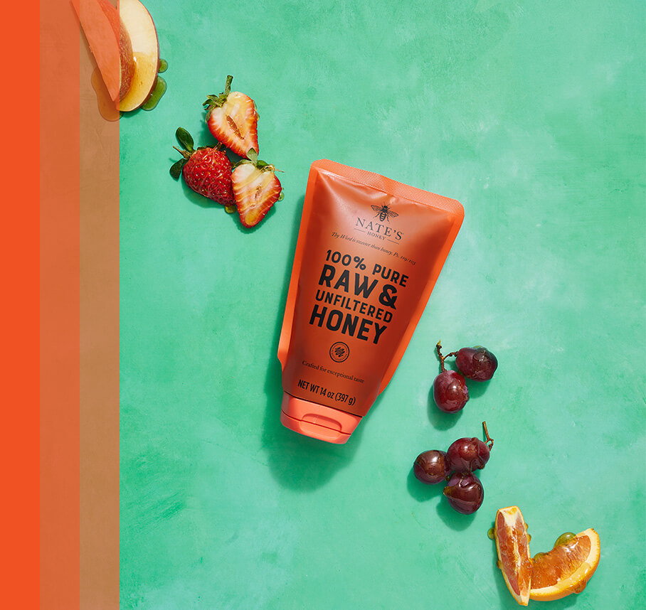 Nate's honey pouch with honey-drizzled fresh fruits on a green background.