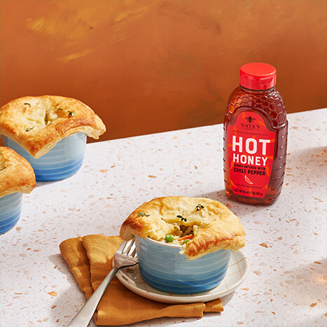 Hot honey chicken pot pie in dish on table next to hot honey bottle.