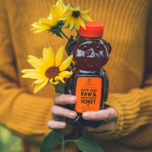 Hands holding a bear-shaped bottle of Nate's honey and a sunflower against a sweater. Hands holding a bear-shaped bottle of Nate's honey and a sunflower against a sweater.