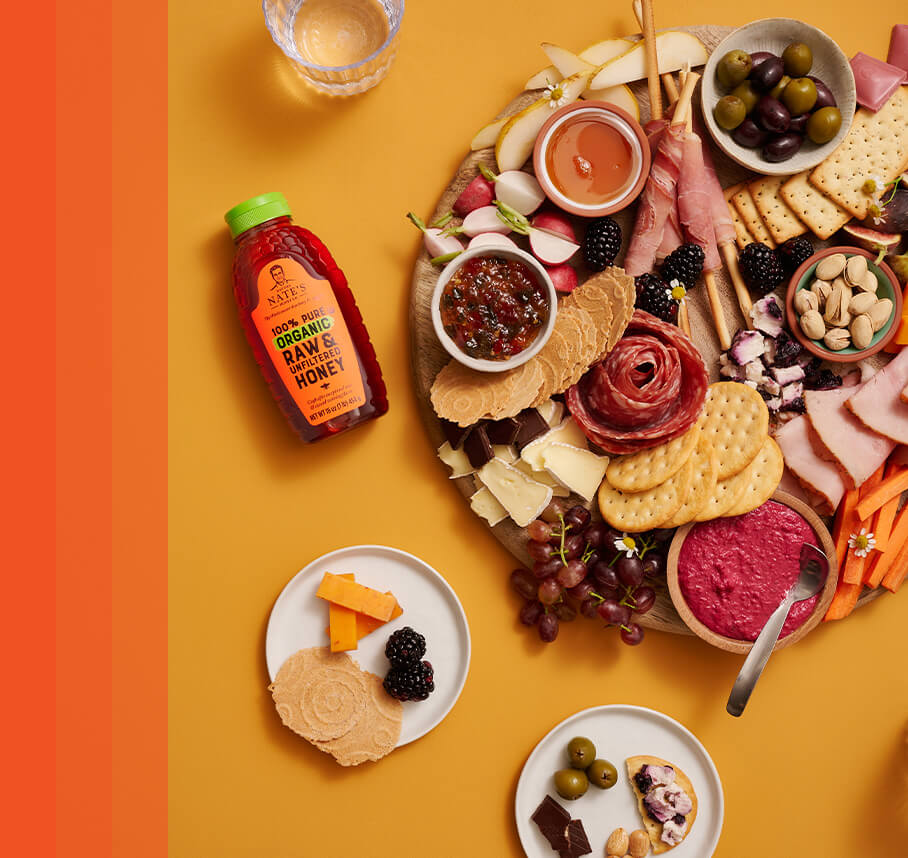 Round charcuterie board assembled with crackers, meats, grapes, olives, cheeses, blackberries and small bowls of dips.