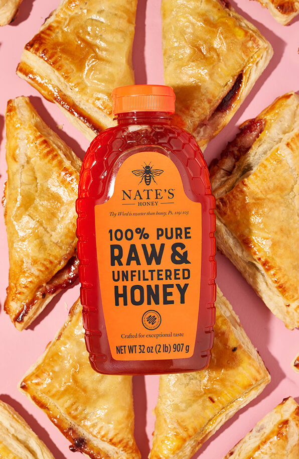 Bottle of Nate's honey with cherry turnovers on a pink backdrop.
