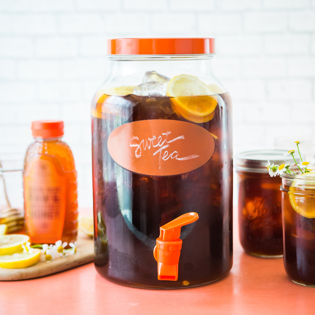 A bright setup featuring a large jar of sweet tea, smaller servings, lemon slices, and a bottle of Nate's Honey.