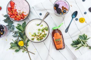 Smoothie bowls with various toppings and a bottle of Nate's organic honey surrounded by green leaves and flowers.