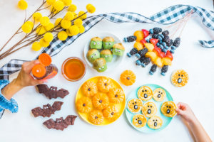 A creative arrangement of fruit and other treats with hands adding honey and decorations, evoking a festive atmosphere.