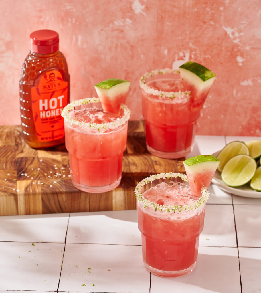 Watermelon cocktails with salted rims, lime garnish, and Nate's Hot Honey bottle.