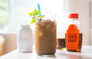 Iced coffee with mint, cream pitcher, and a honey bottle on a bright table.