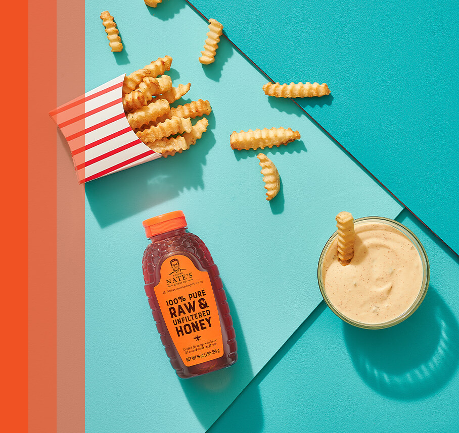 Red and white striped container of crinkle cut French fries displayed next to Nate's honey bottle and dipping ramekin.
