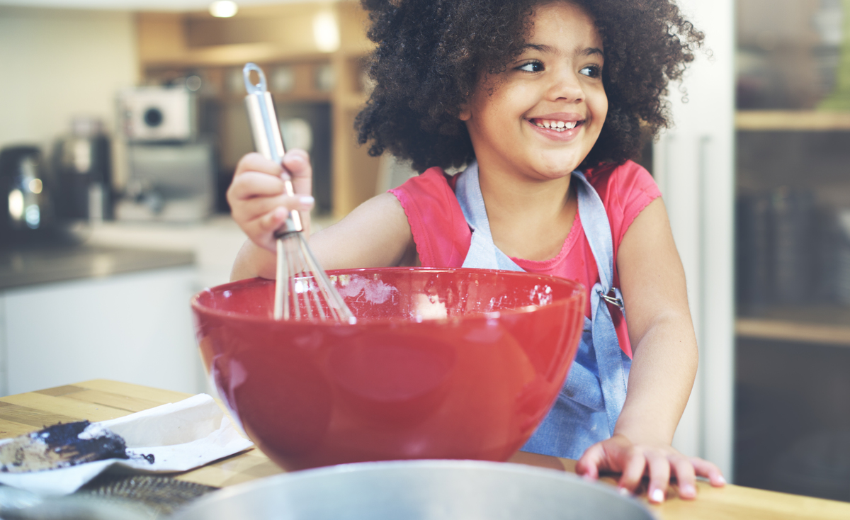 Happy child whisking in a red bowl in a kitchen.