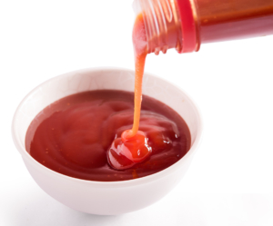 Ketchup pouring into a bowl on a white background. Ketchup pouring into a bowl on a white background.