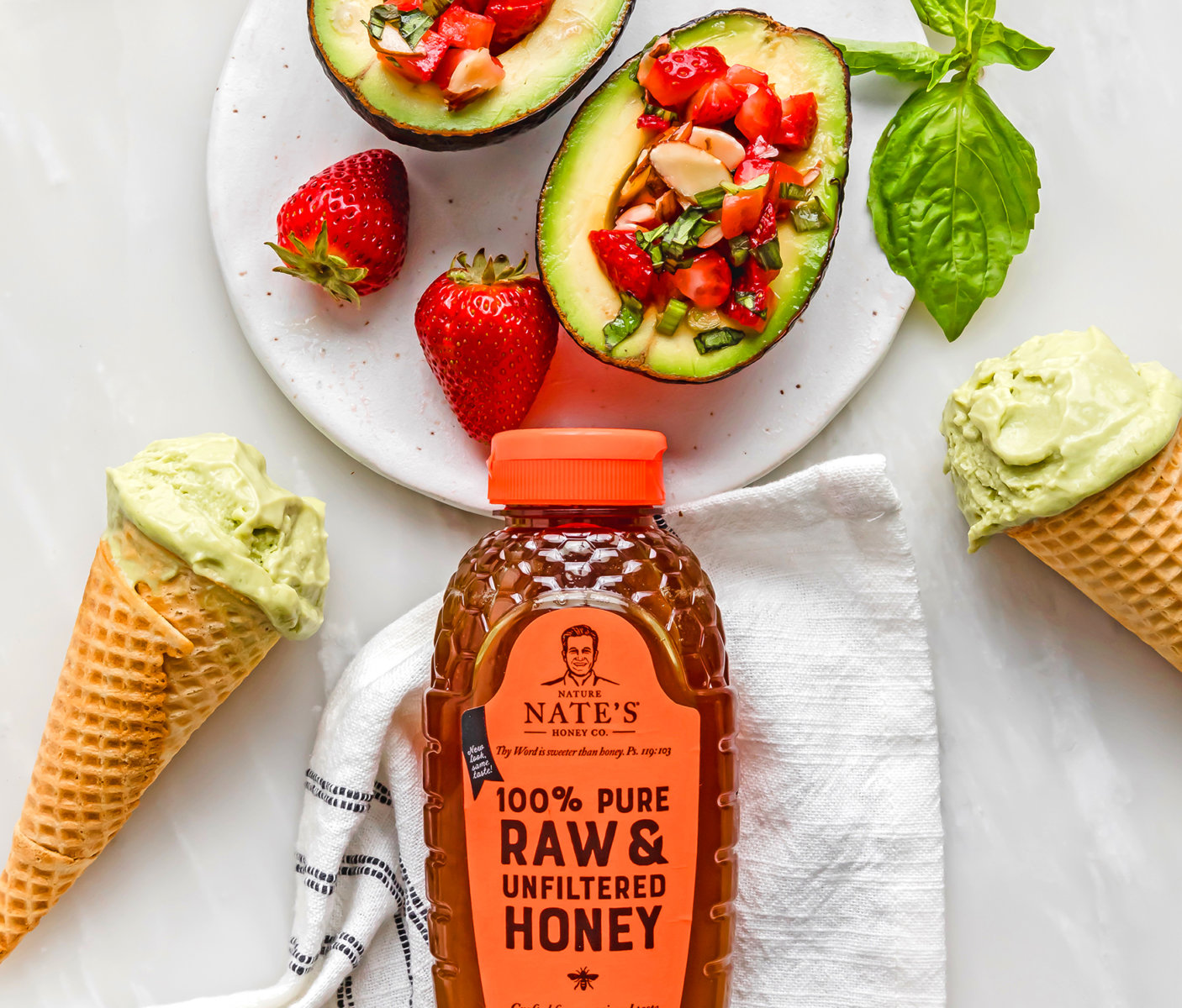 Avocado halves filled with diced fruit, a bottle of Nate’s honey, avocado ice cream cones, and fresh strawberries.
