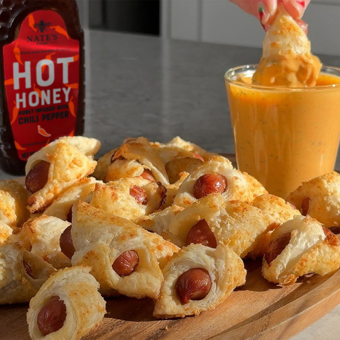 Nate’s Hot Honey with pigs in a blanket on a wooden board, served with a hot honey dipping sauce.