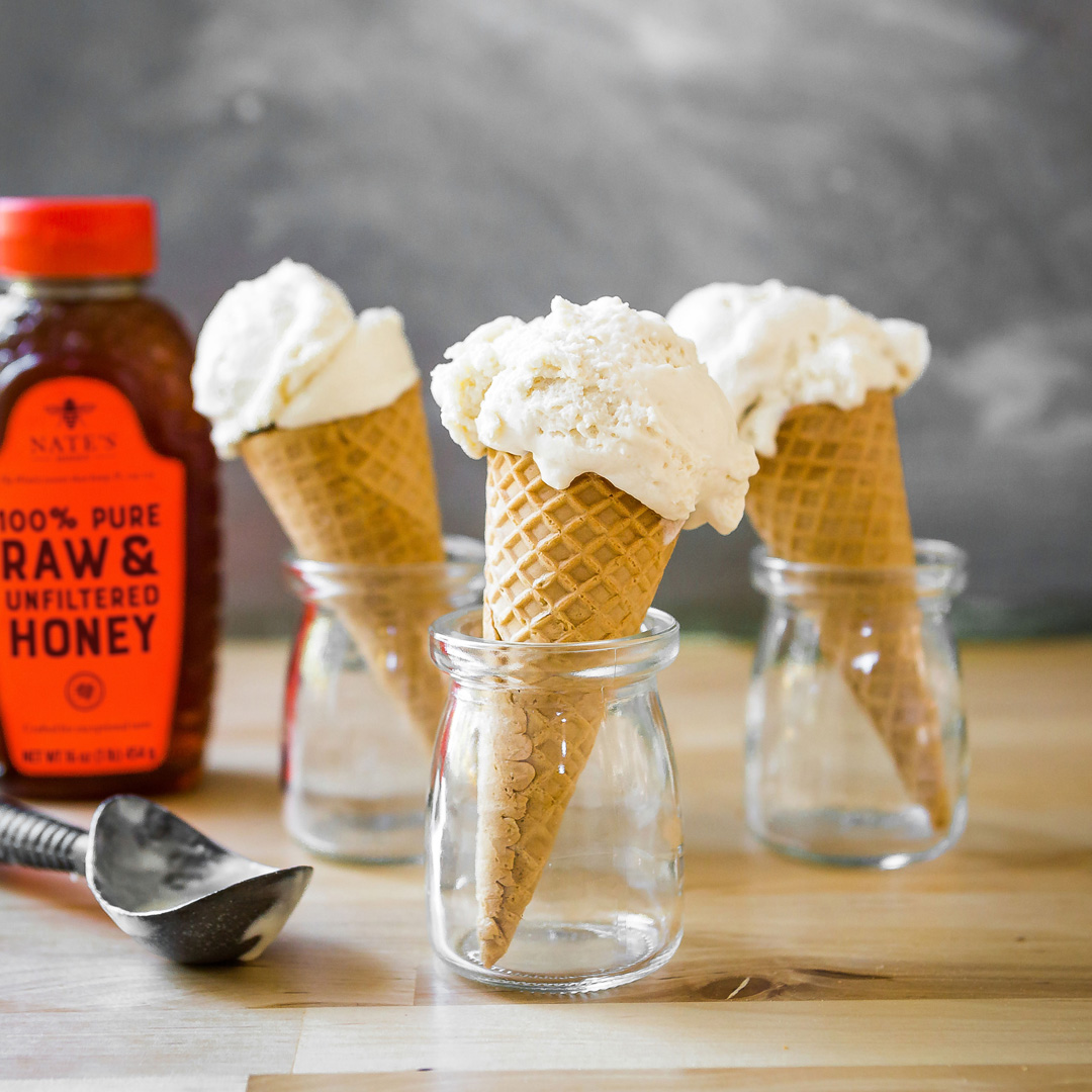 Vanilla ice cream cones in jars with Nate's Honey bottle and scoop on a wooden table.