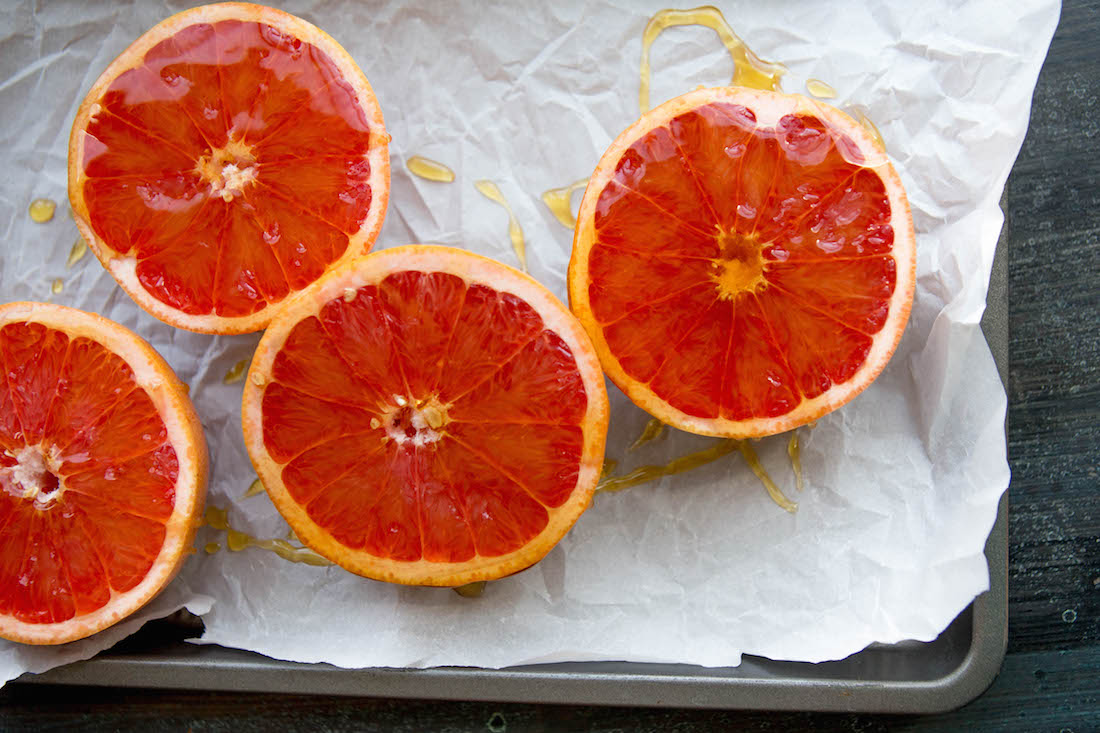 Grapefruit halves with honey drizzle on parchment paper.