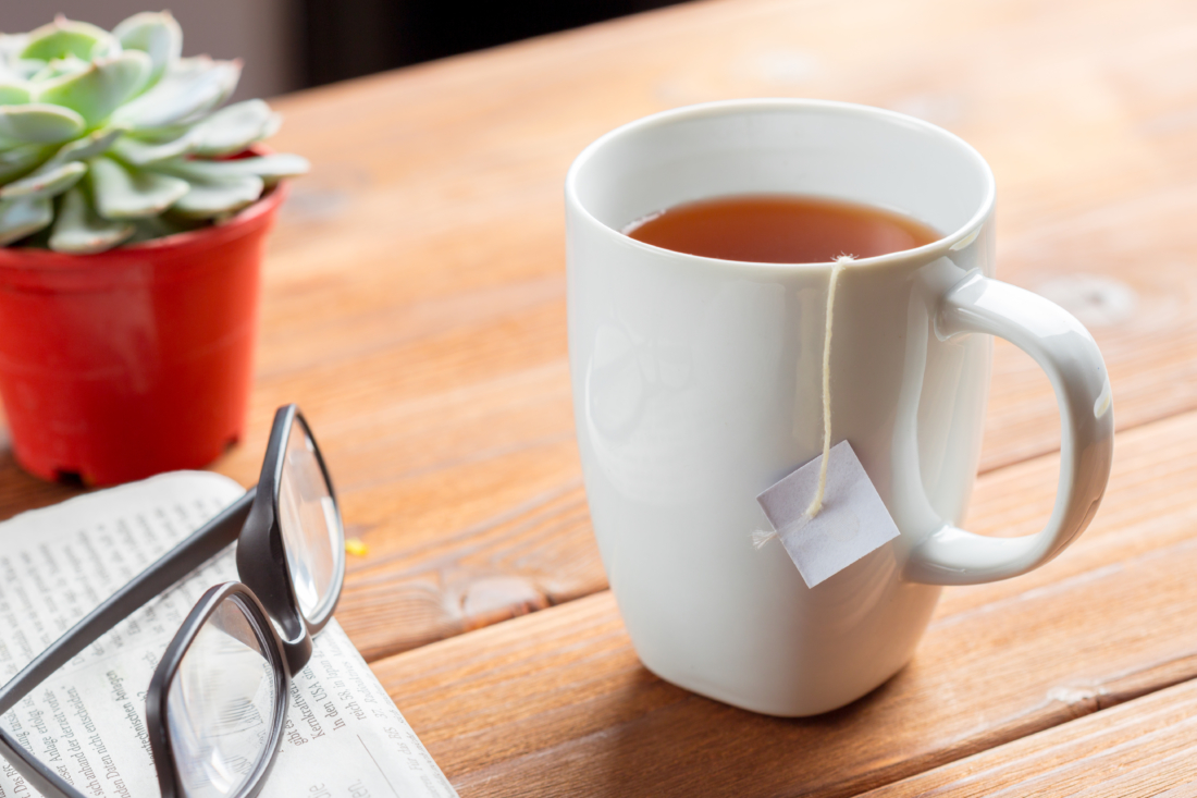 Teacup with teabag, glasses, and plant on a wooden table.