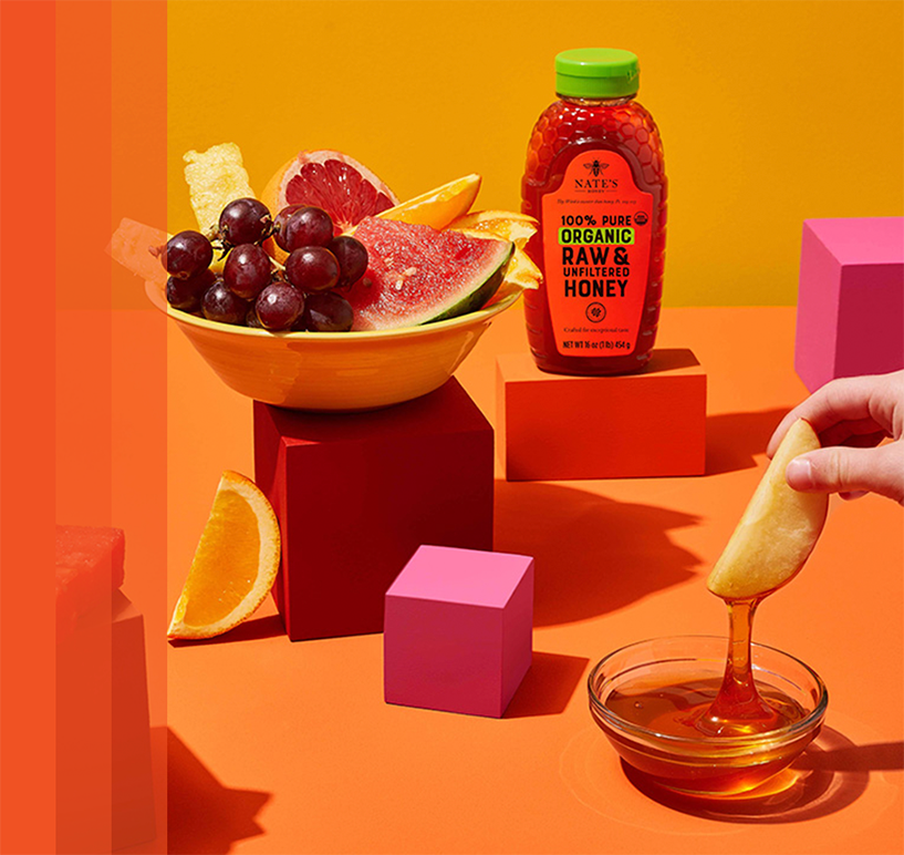 Fruit in bowls next to organic honey bottle.