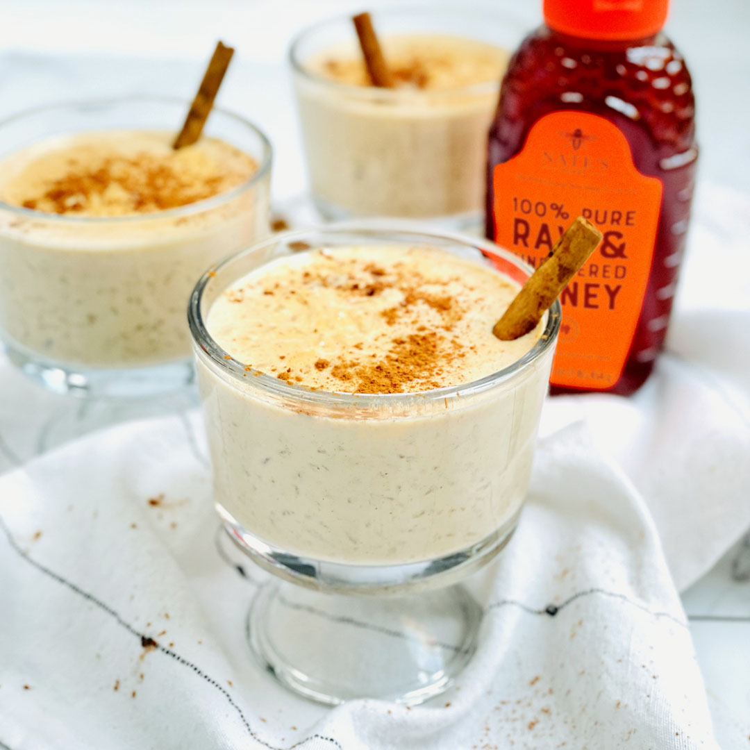 Creamy rice pudding in glasses with cinnamon, a bottle of Nate’s Honey with an orange cap in the backdrop.