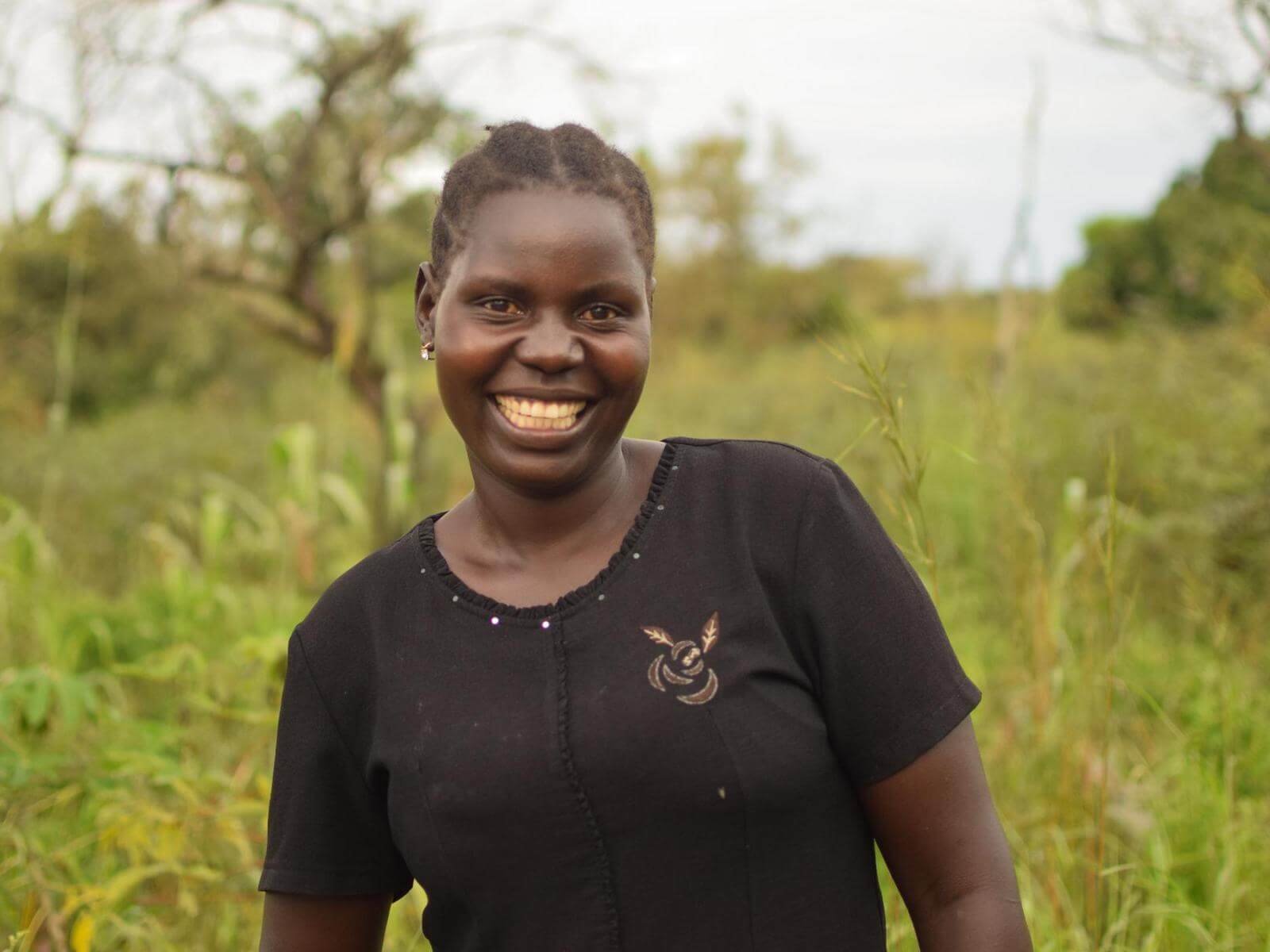A smiling woman in a black shirt with a nature backdrop.