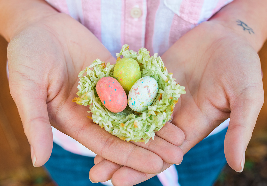 Hands cradling a coconut nest with candy Easter eggs, symbolizing spring and renewal.