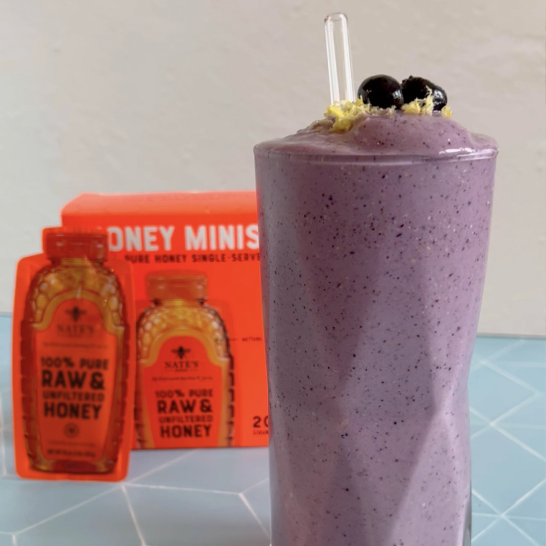 A purple blueberry smoothie garnished with blueberries, next to Nate's honey Minis.