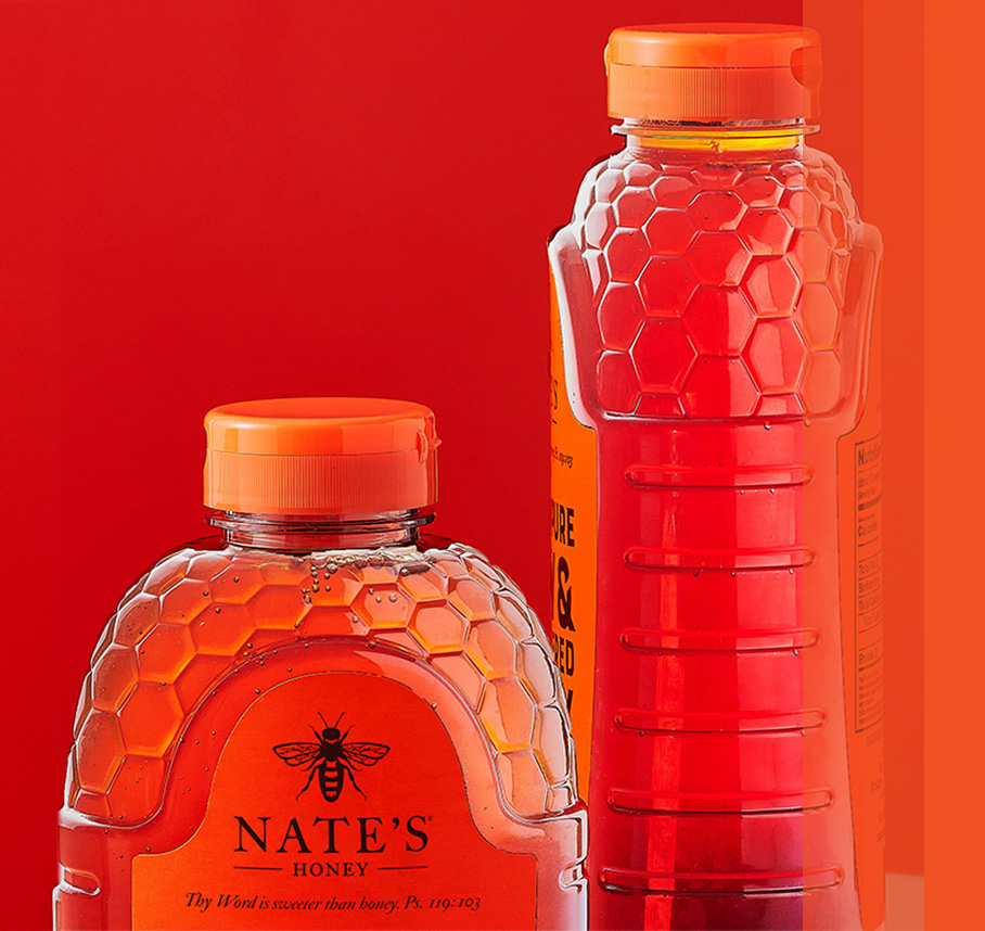 Two Nature Nate's honey bottles with honeycomb designs on a red background.