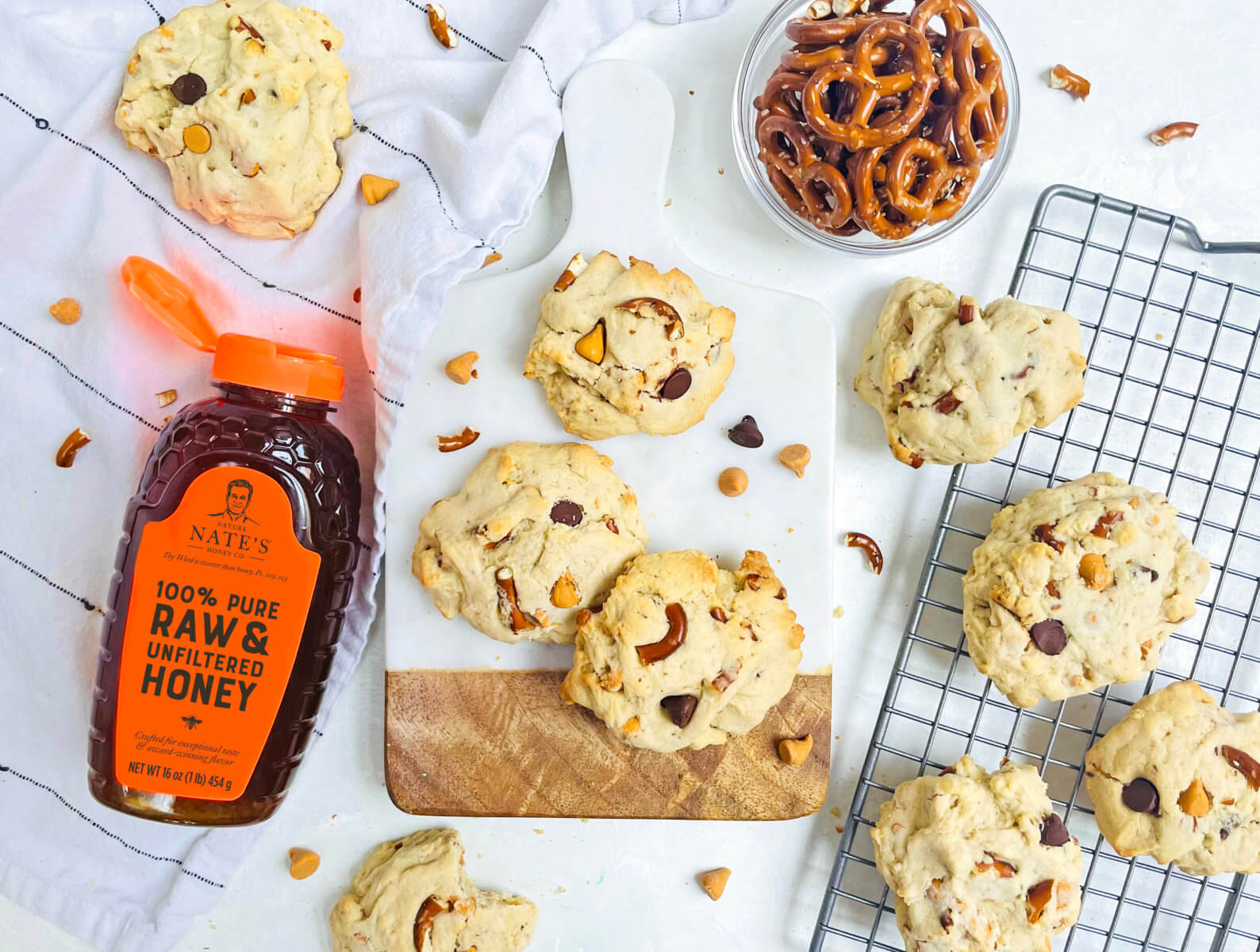 Butterscotch pretzel honey cookies on wire rack, bowl of pretzels and a bottle of Nate's honey on a cloth.