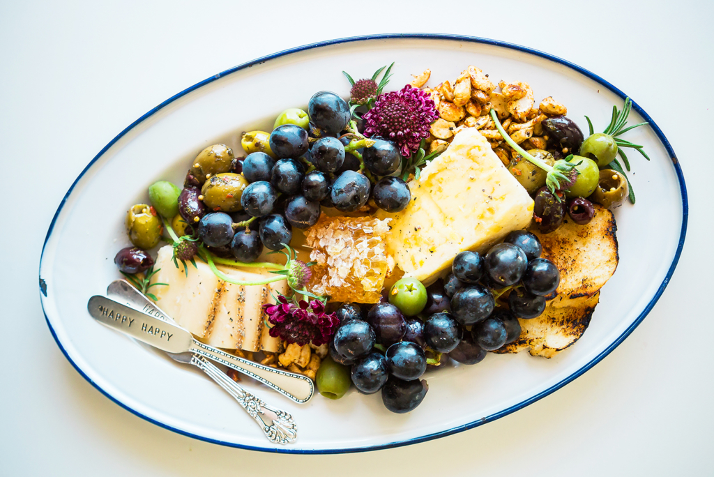 Cheese platter with fruits, olives, honeycomb and nuts on a decorated plate.