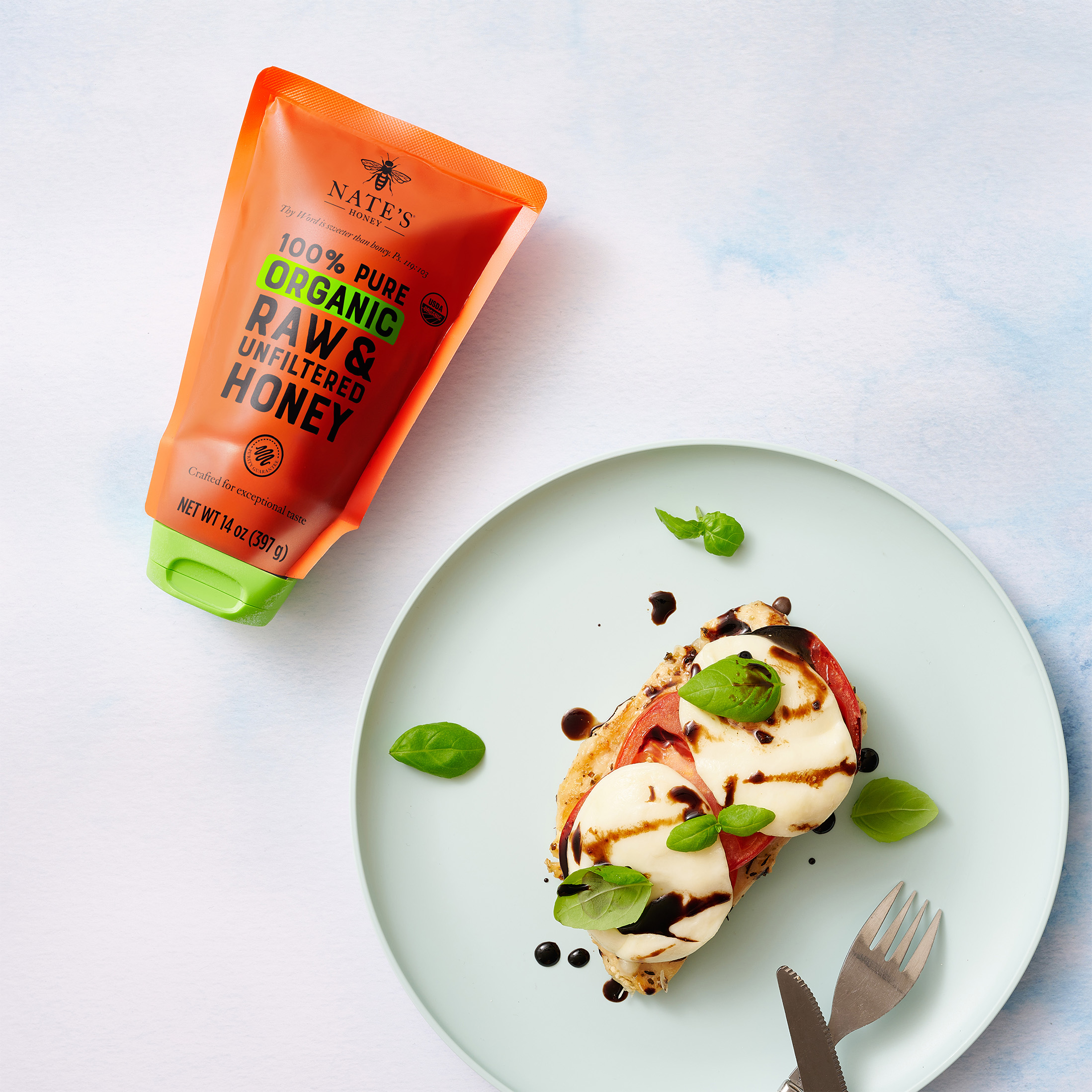 Nate's Organic Honey pouch next to plate with honey balsamic glazed caprese chicken and silverware.