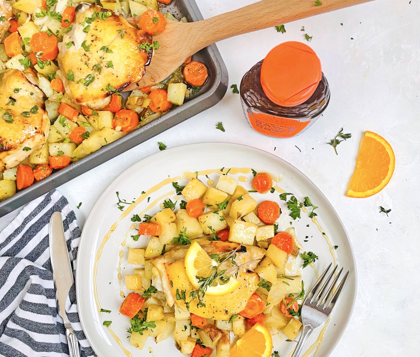 Roasted chicken and vegetables garnished with lemon in a sheet pan and served on a plate with a Nate’s honey bottle.