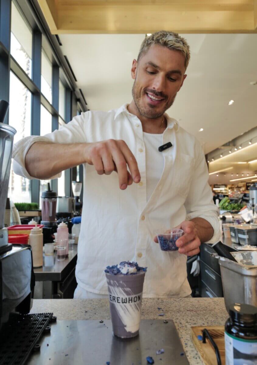 Chris Appleton preparing a purple layered smoothie made with honey at a bar with an EREWHON cup.