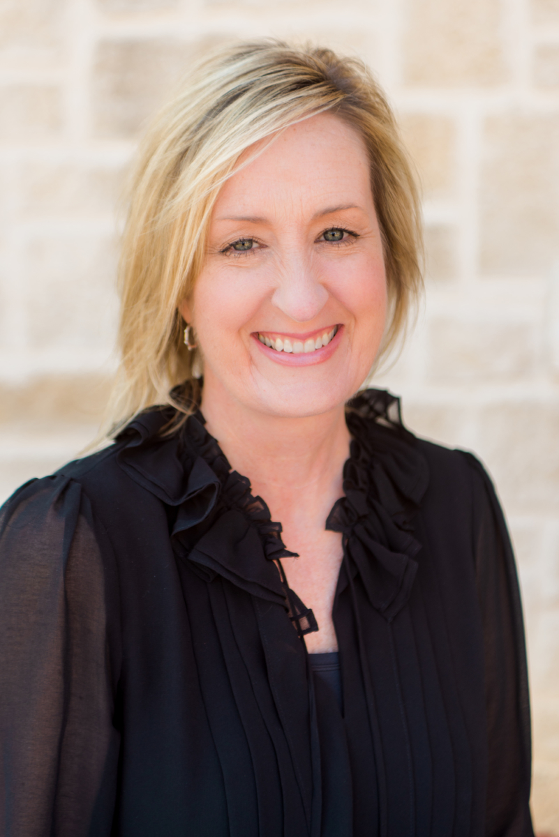 Female Nate's employee smiling in a black ruffled blouse against a stone wall.