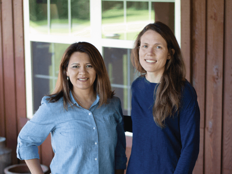 Two Nate's employees smiling in casual attire standing on a porch.