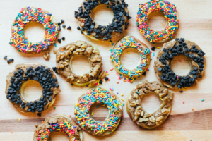 Apple rings topped with nut butter, chocolate chips, sprinkles and nuts on wood.
