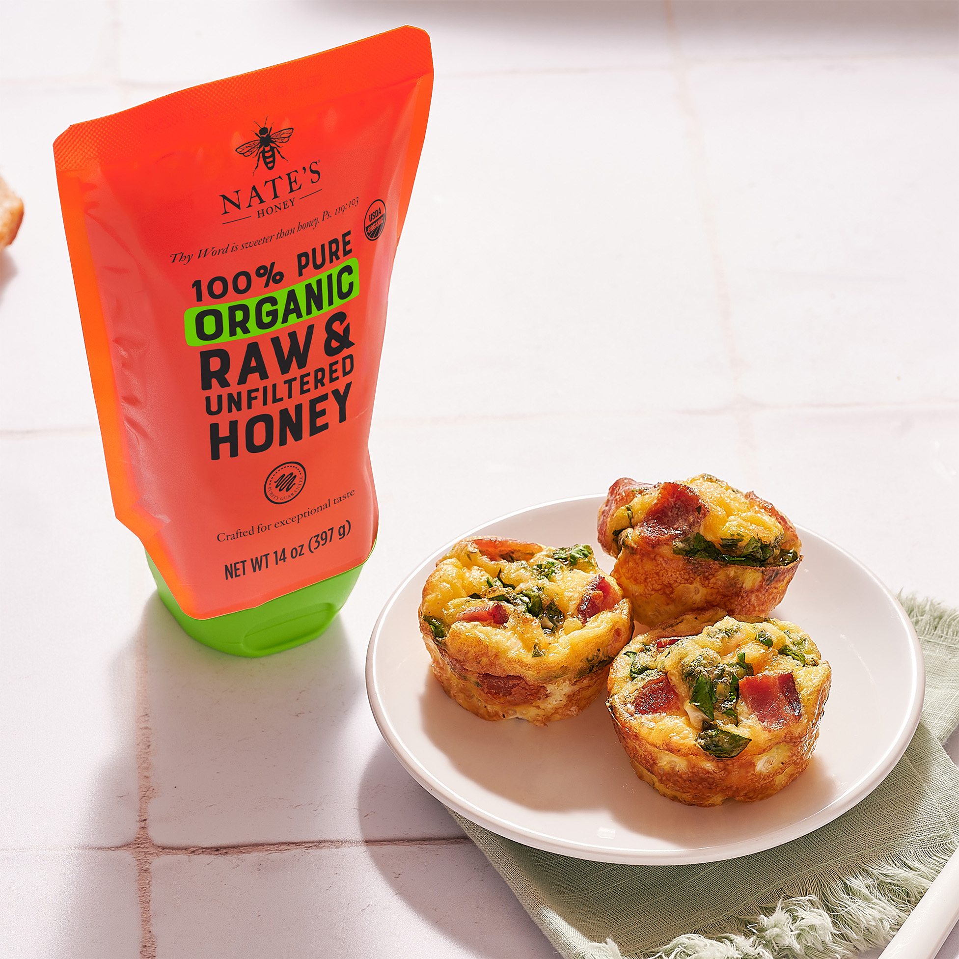 Nate's Organic Honey pouch next to plate of egg bites on white tile background.