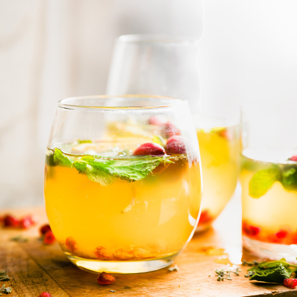 Golden-hued beverage with mint leaves and pomegranate seeds with an inviting ambience. Golden-hued beverage with mint leaves and pomegranate seeds with an inviting ambience.