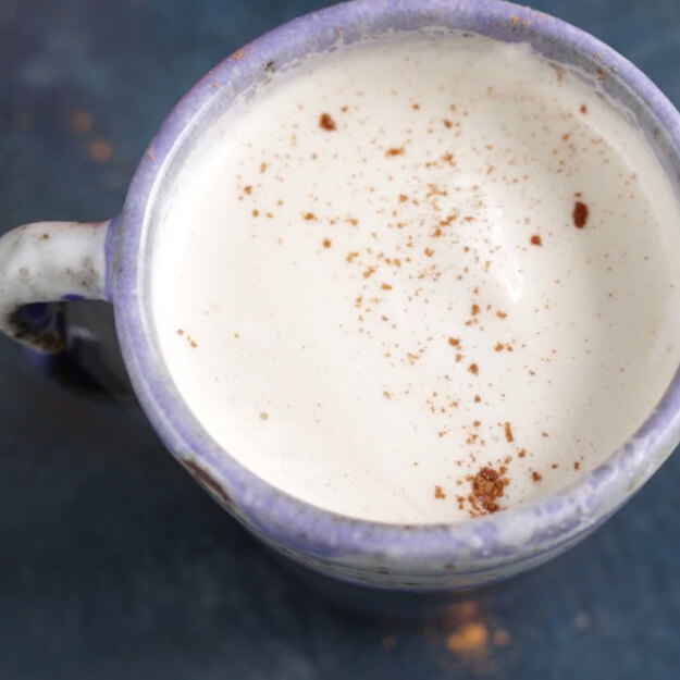Top view of a mug of fauxpaccino sprinkled with cinnamon on a blue surface.