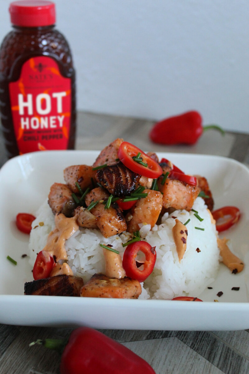 Firecracker Salmon Bites cooked with Nate’s Hot Honey on a bed of white rice garnished with chives and red chili peppers.