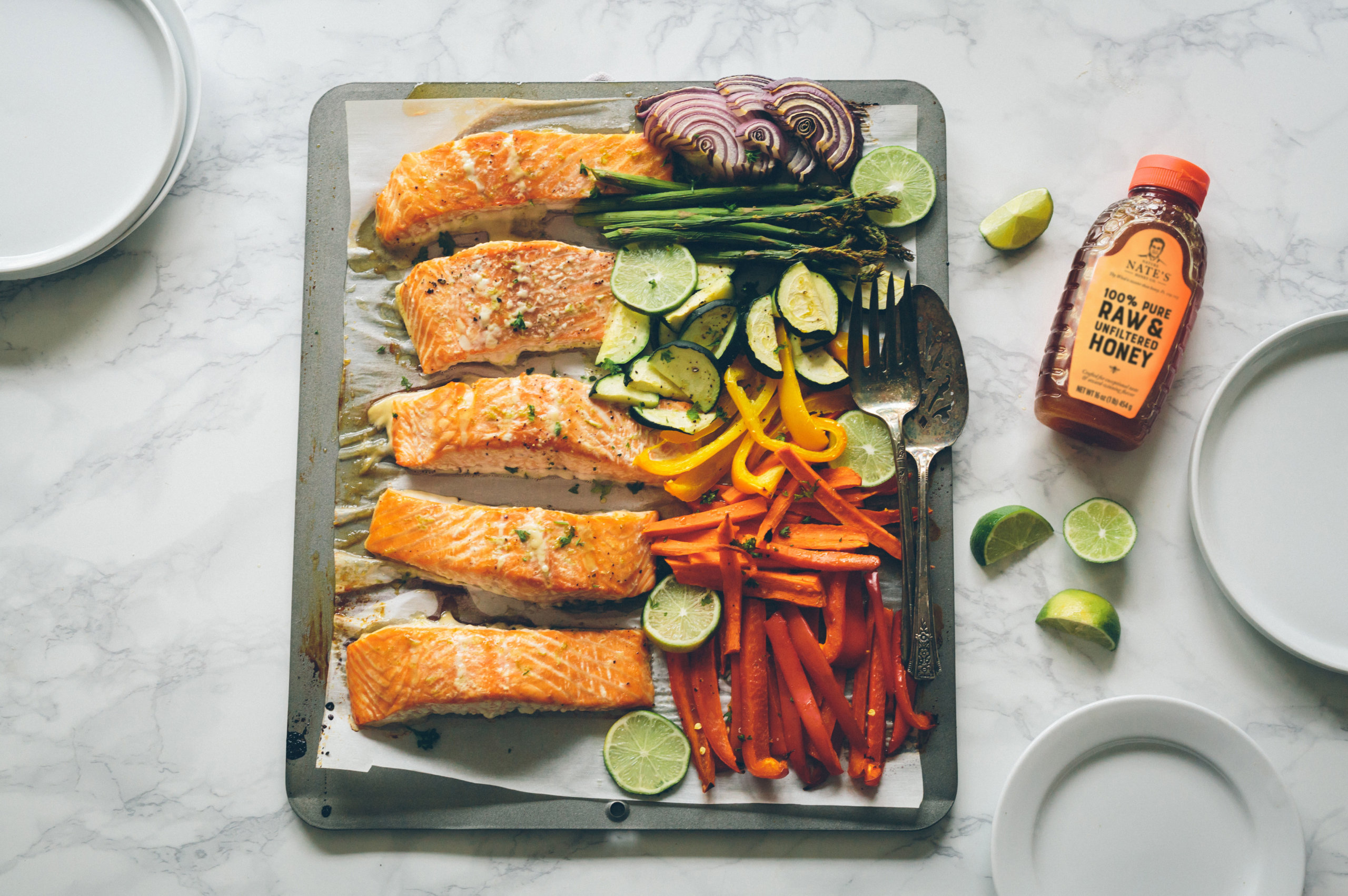 Salmon fillets and roasted vegetables on a sheet pan with a bottle of Nate's honey on the side.