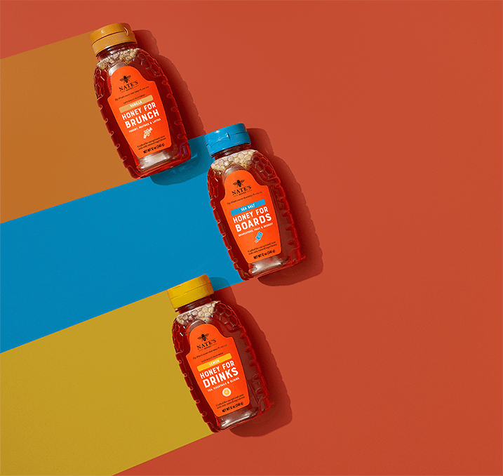 Three bottles of Nate’s Flavored Honey — Honey for Brunch, Honey for Boards and Honey for Drinks — arranged on a colorful striped background.