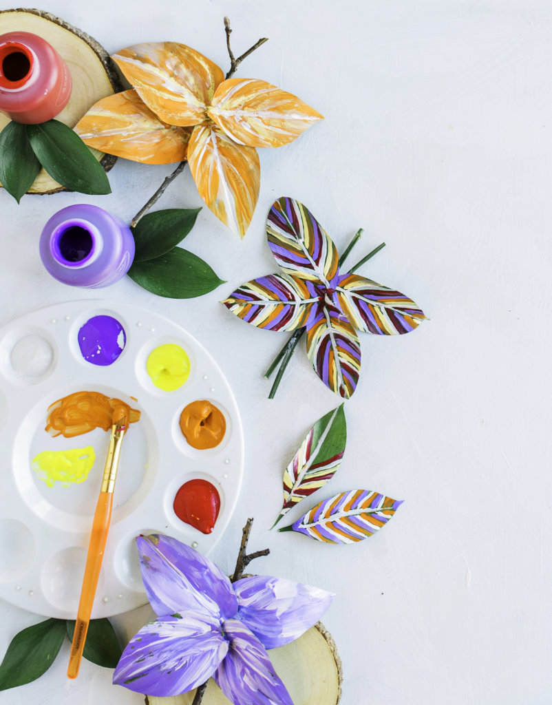 Crafting with painted paper butterflies, flowers, paint pots and brush on a white surface.