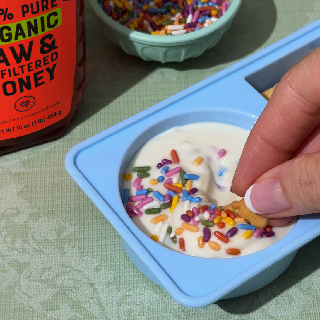 Hand dipping graham cracker into Funfetti Cake Batter Yogurt Dip.
