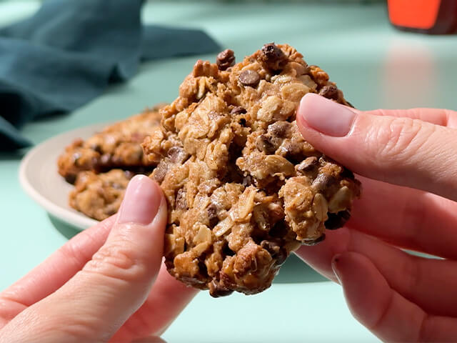 Hands holding chocolate and oats cookie in a pull apart fashion.
