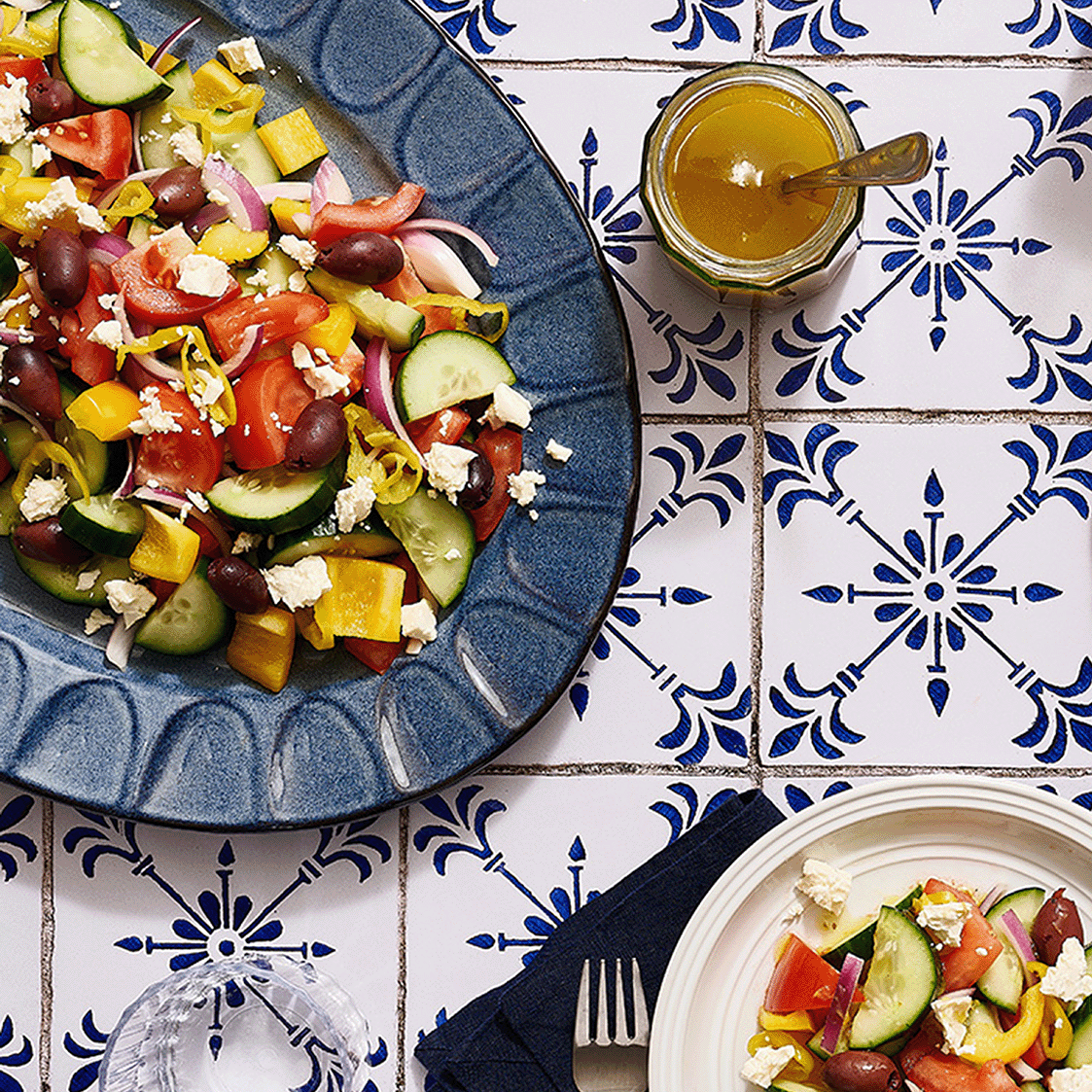 Greek salad on blue plate next to small bowl of dressing.